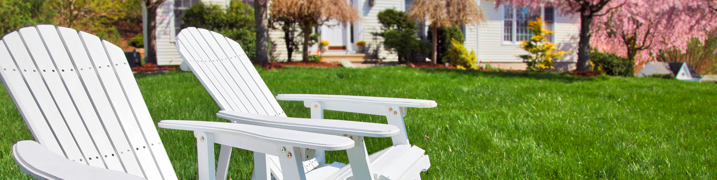 spring image - white house with blooming spring plantings out front and two white adirondack chairs sitting on a beautiful lawn