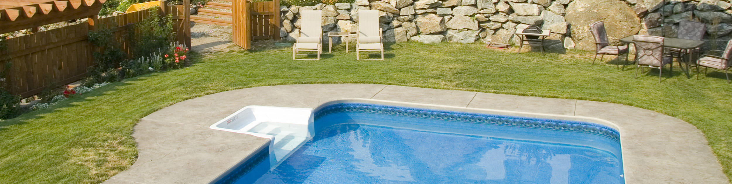 view of backyard with built in swimming pool, lawn furniture and stone wall