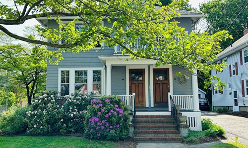 light blue multi-family home with white trim and pretty hedges out front; a double door entry is covered