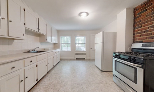 kitchen with white cabinets, white refrigerator, stainless steel stove with brick behind it
