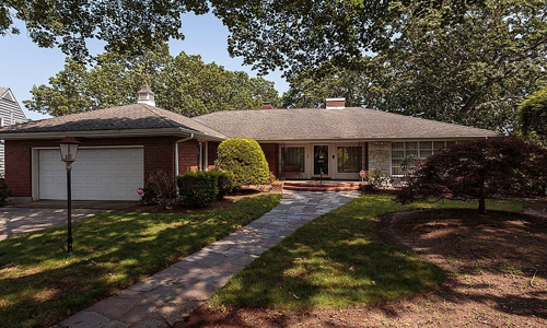 ranch style home with partial brick front, a white garage door and lots of hedges and trees in view