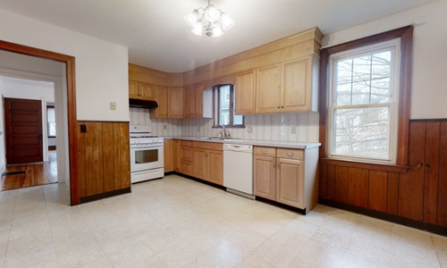 empty kitchen with light tile floor, half panel walls with white paint above, white appliances and light cabinets