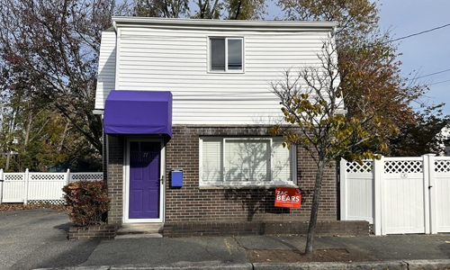 single family colonial style home with a partial brick front, a purple door covered by a purple awning and a fenced yard