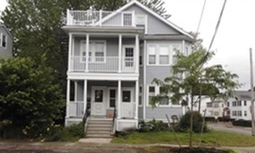 light gray multi family home with white trim and doors; there are covered porches on the first and second floor and a balcony on the third