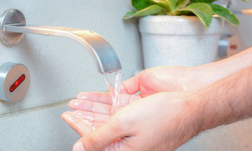 Hands washing under touchless faucet.