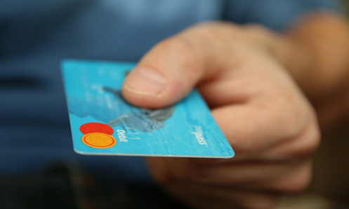 a hand holding out a blue credit card with orange and red circles on it