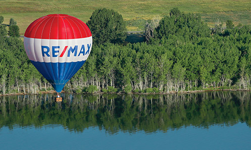 REMAX balloon floating over a body of water with trees in the background
