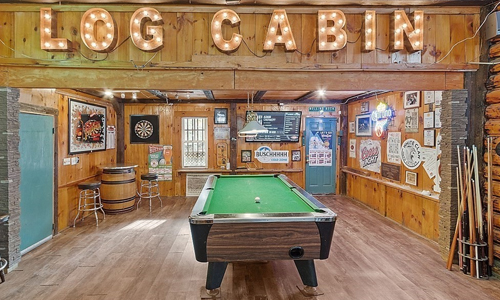 a gaming room with a pool table and dart board visible; a large lighted sign saying Log Cabin is on the wall along with many other signs