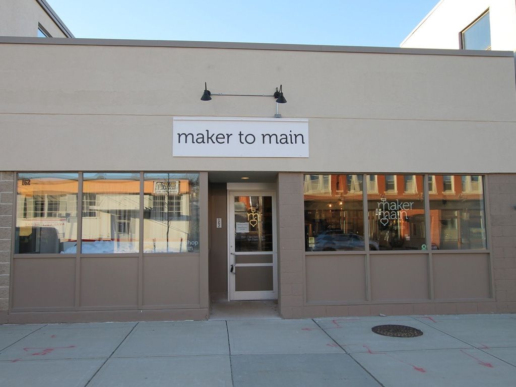 Tan building with lots of windows on the front and a sign that reads Maker to Main
