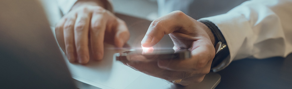 hands using cell phone with laptop in view