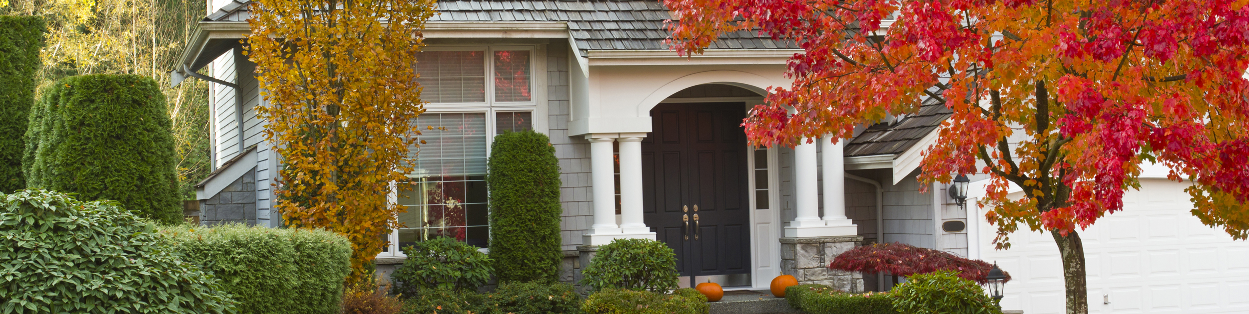 exterior view of home with gray shingles, brown double doors and Fall foliage surrounding the home