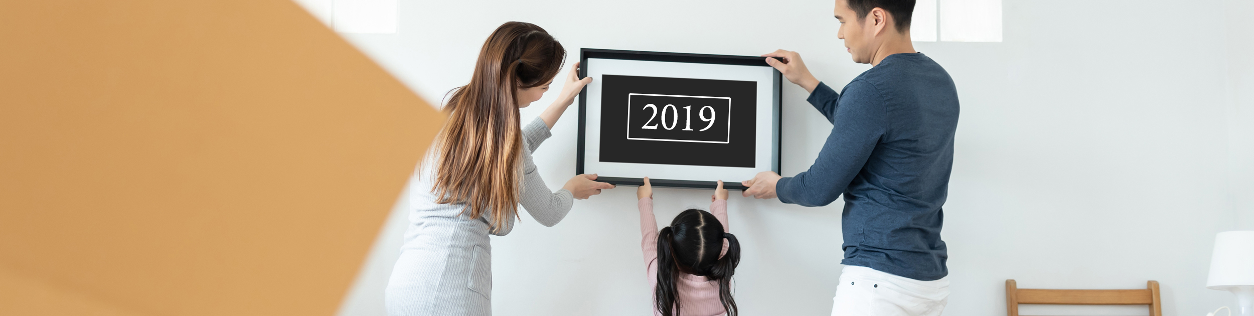 couple with young girl hanging a framed 2019 sign on the wall