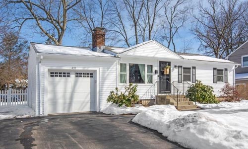 three bedroom white ranch for sale in Norwood, MA - front yard is covered in thick snow, the home has white aluminum siding, a dark door and shutters, a single garage and chimney