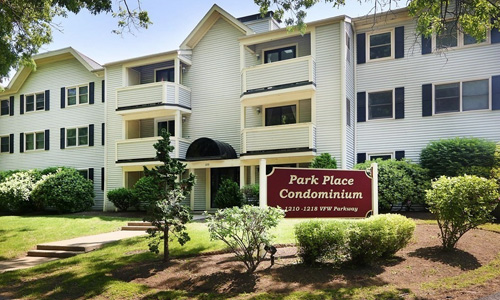 large multi unit white condominium building with black shutters, lots of balconies and a sign out front that reads Park Place Condominium
