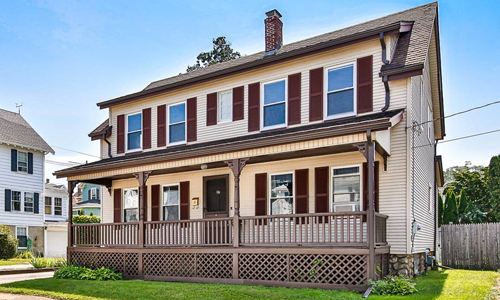 Tan colonial style home in Gloucester MA with brown shutters, door and deck out front.