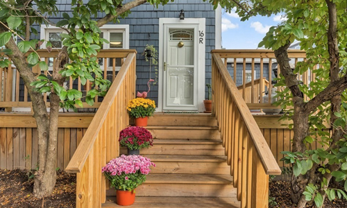 wooden outside staircase with multiple colored mums on the stairs leading up to a blue building with a white door showing 16R on it