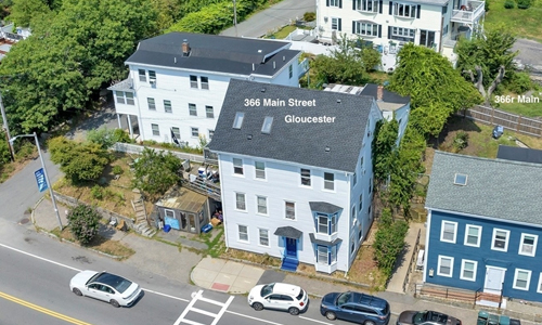 white 3 story 3 family home with a covered entrance and 2 skylights seen on the roof; other homes are nearby